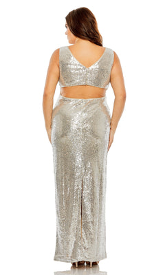 A woman stands facing away in the Long Plus-Size Formal Dress 68538 by Mac Duggal, a sleeveless, floor-length silver gown featuring a V-back, cut-out waist, and back slit.