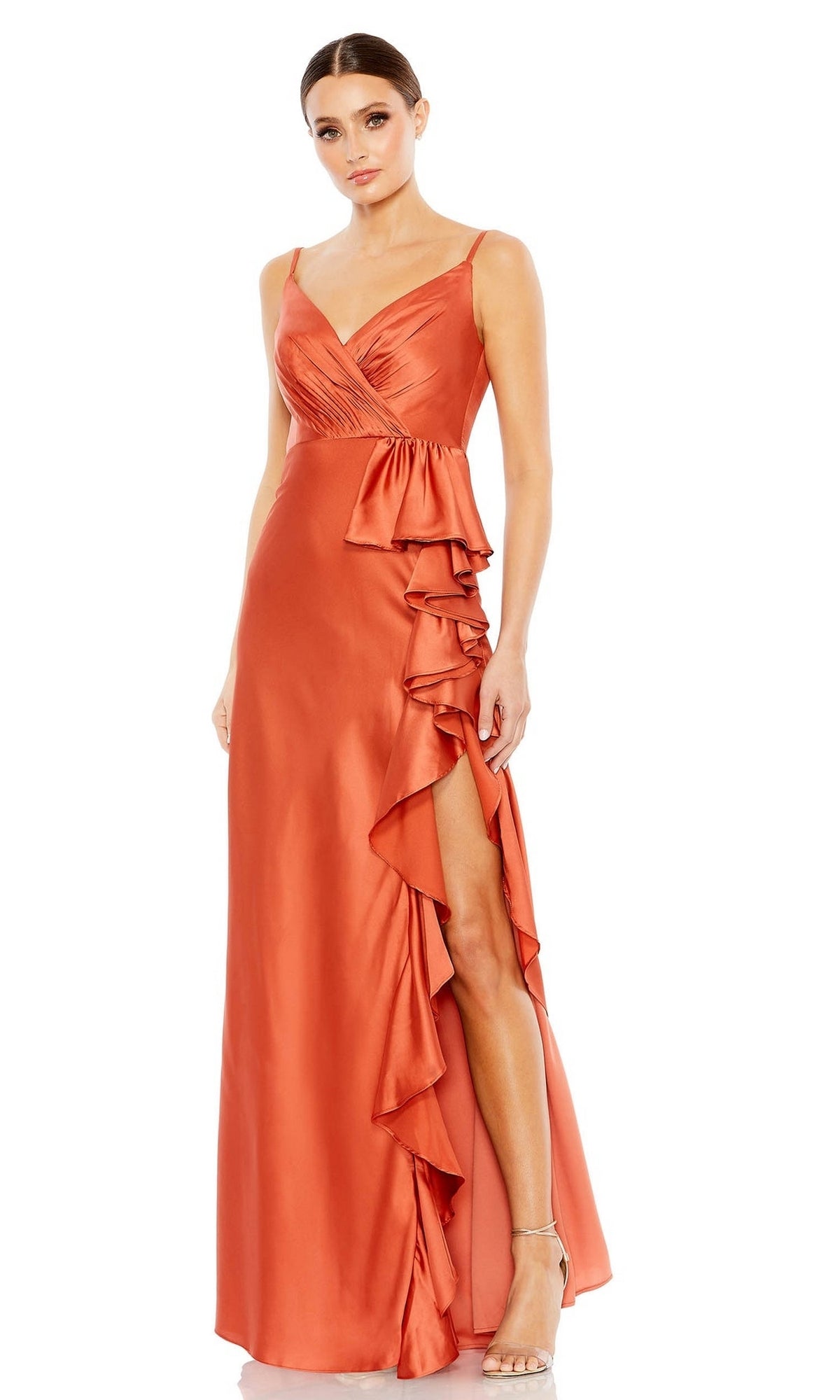 A woman stands in heels wearing the Mac Duggal Long Formal Dress 68551—an orange, sleeveless satin gown with a V-neckline, ruffled side detail, floor-length design, and high slit.