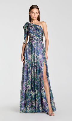 A woman poses against a plain background in the Mac Duggal 68553, a one-shoulder floral formal gown with a thigh-high slit, embodying modern elegance.