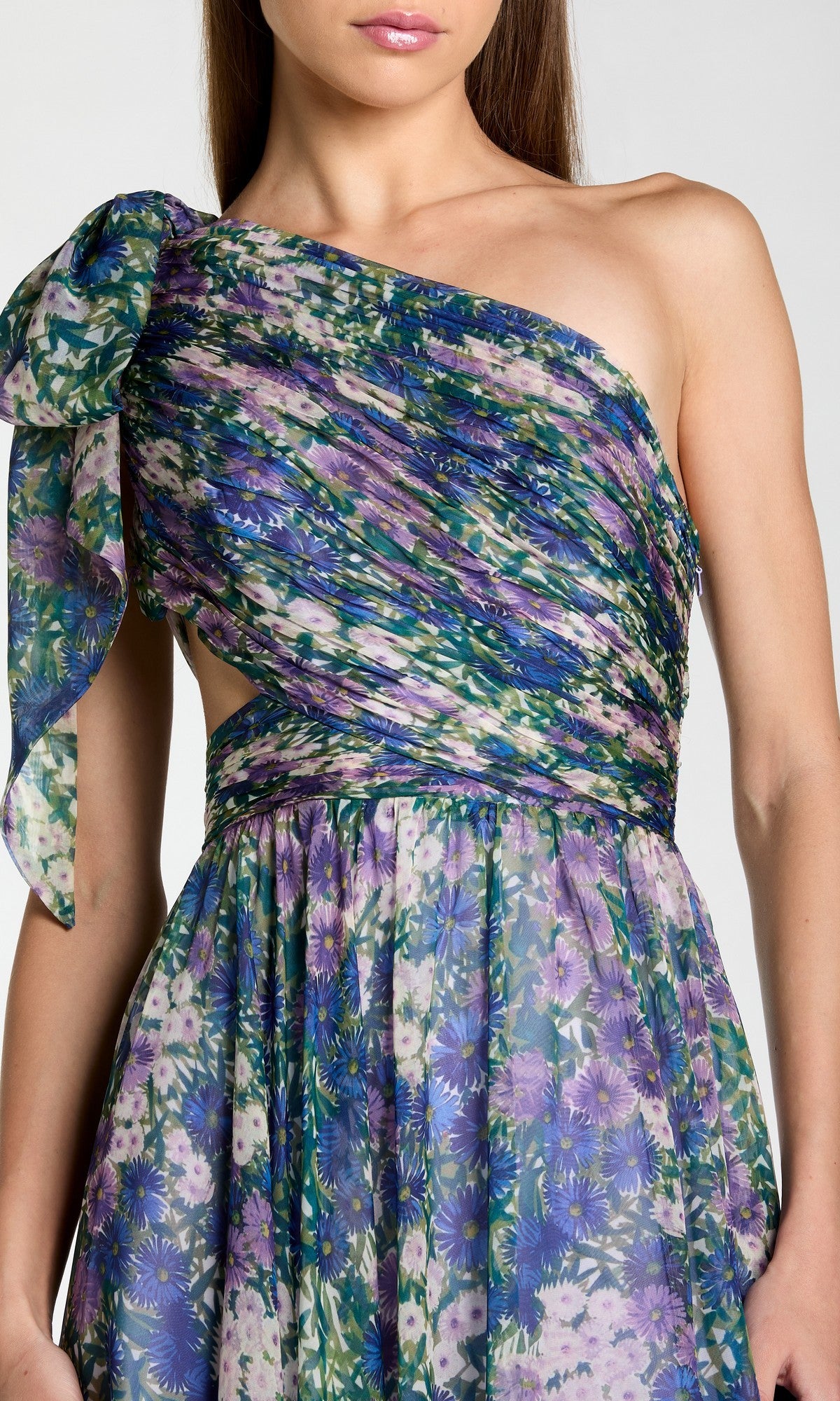 A person wearing the Mac Duggal 68553 One-Shoulder Floral Formal Gown in blue, green, and purple, featuring a gathered bodice and a bow accent on the shoulder.