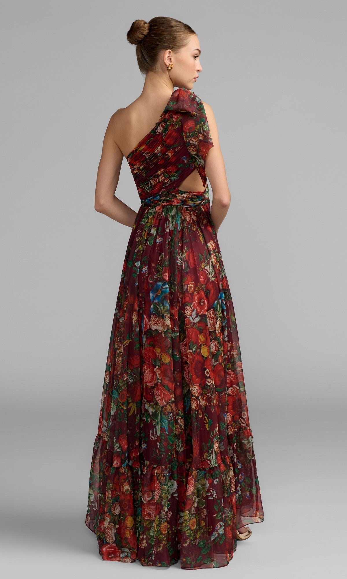 A woman poses against a plain grey background in the Mac Duggal 68553 One-Shoulder Floral Formal Gown, featuring a floor-length silhouette and a back cutout detail.