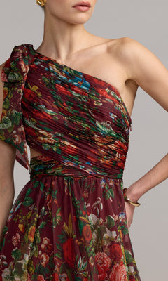 A woman in the Mac Duggal 68553 One-Shoulder Floral Formal Gown, featuring a colorful burgundy floral pattern, gathered fabric detail, and elegant styling.