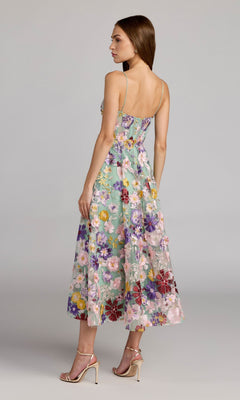 A woman wearing the Tea-Length Party Dress: Mac Duggal 68605, a sleeveless floral midi dress with a structured bodice and a graceful A-line skirt, paired with strappy high heels, stands and looks to the side against a plain background.