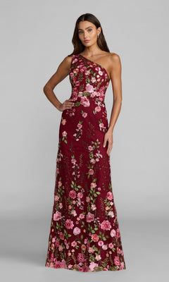 A woman stands against a plain gray background wearing the Mac Duggal 68606 Long Floral-Print Formal Dress, a sleeveless, floor-length maroon maxi with pink and green floral embroidery.