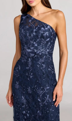A woman models the Long Floral-Print Formal Dress: Mac Duggal 68606, featuring a navy blue one-shoulder design with elegant floral embroidery, set against a plain gray background.