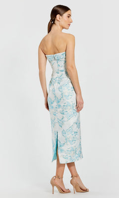 A woman stands in profile against a plain background wearing the Floral Midi Party Dress: Mac Duggal 68621, a pale blue floral brocade sheath dress, paired with beige high-heeled sandals.