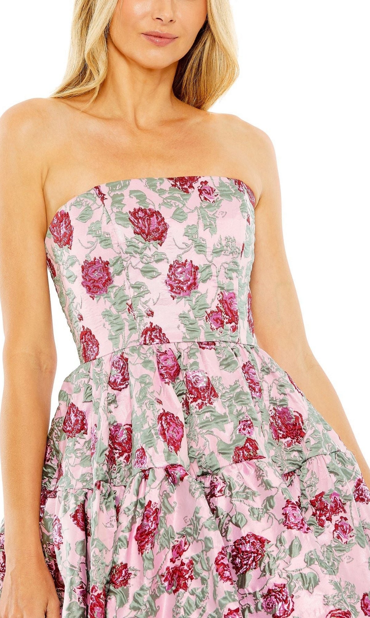 A woman wears the Short Pink Floral Dress 68624 by Mac Duggal, featuring a strapless fitted bodice, layered skirt, and vibrant red and green floral print on a pink base for an elegant party look.