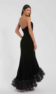 A woman models the Mac Duggal 68697 long formal dress, featuring a strapless velvet bodice, tulle ruffle hem detailing, and a thigh-high slit, as she poses looking over her shoulder against a plain background.