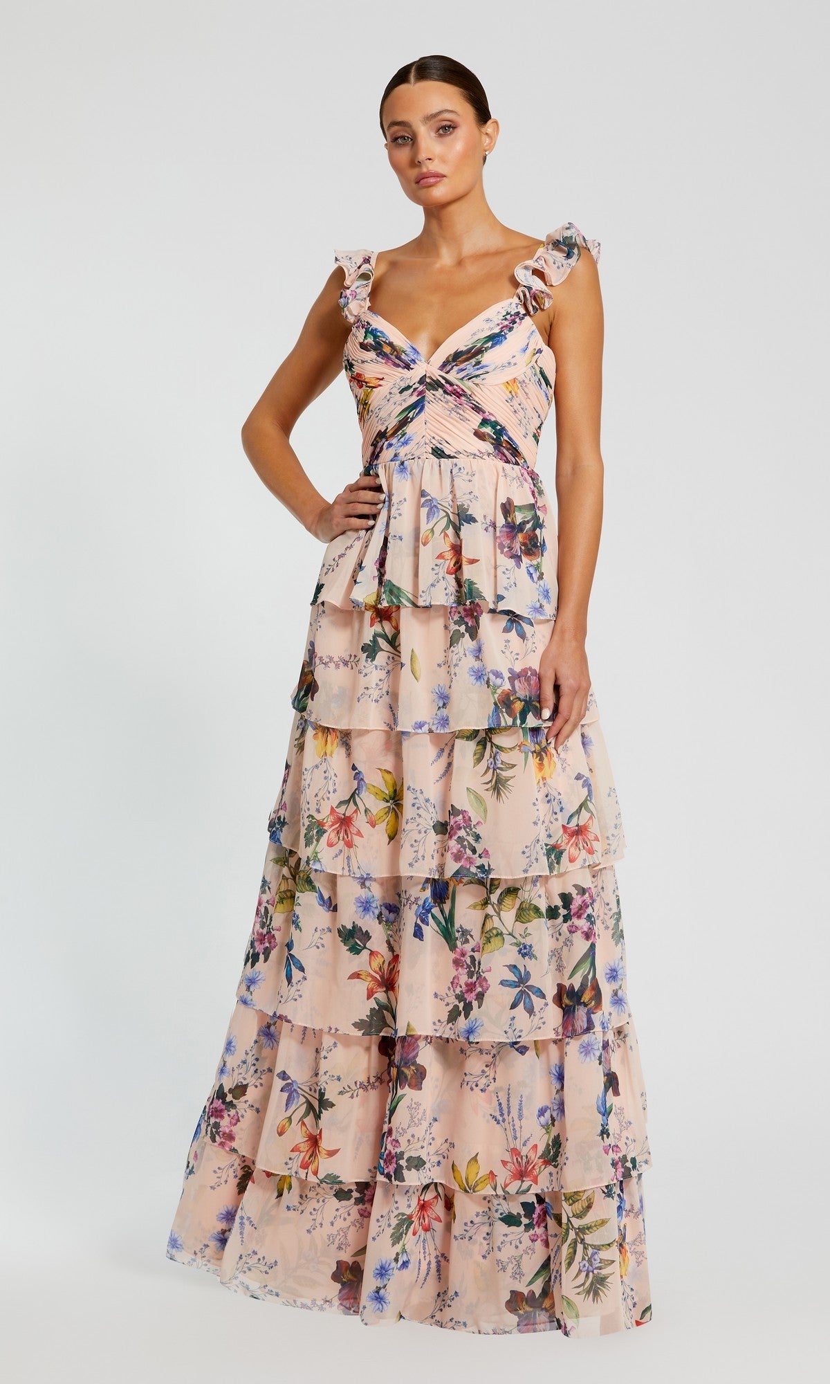 A woman stands against a plain white background wearing the Mac Duggal 68742 long formal dress in Pink Multi, featuring sleeveless floral chiffon and a ruffle-tiered floor-length skirt.