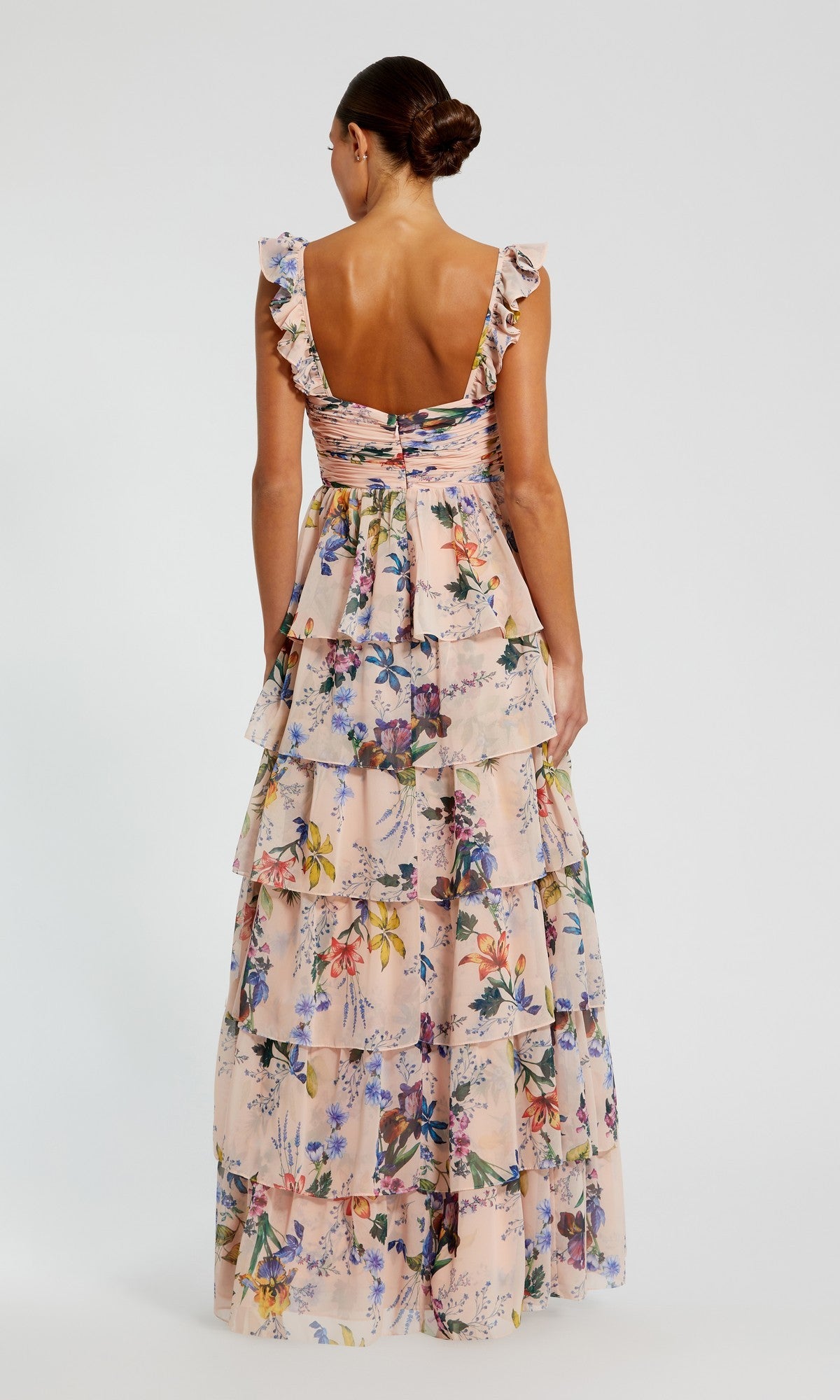 A woman faces away, wearing the Mac Duggal 68742 Long Formal Dress—a floor-length floral chiffon gown with ruffled straps, a ruched bustier bodice, and a tiered skirt elegantly cascading down her back.
