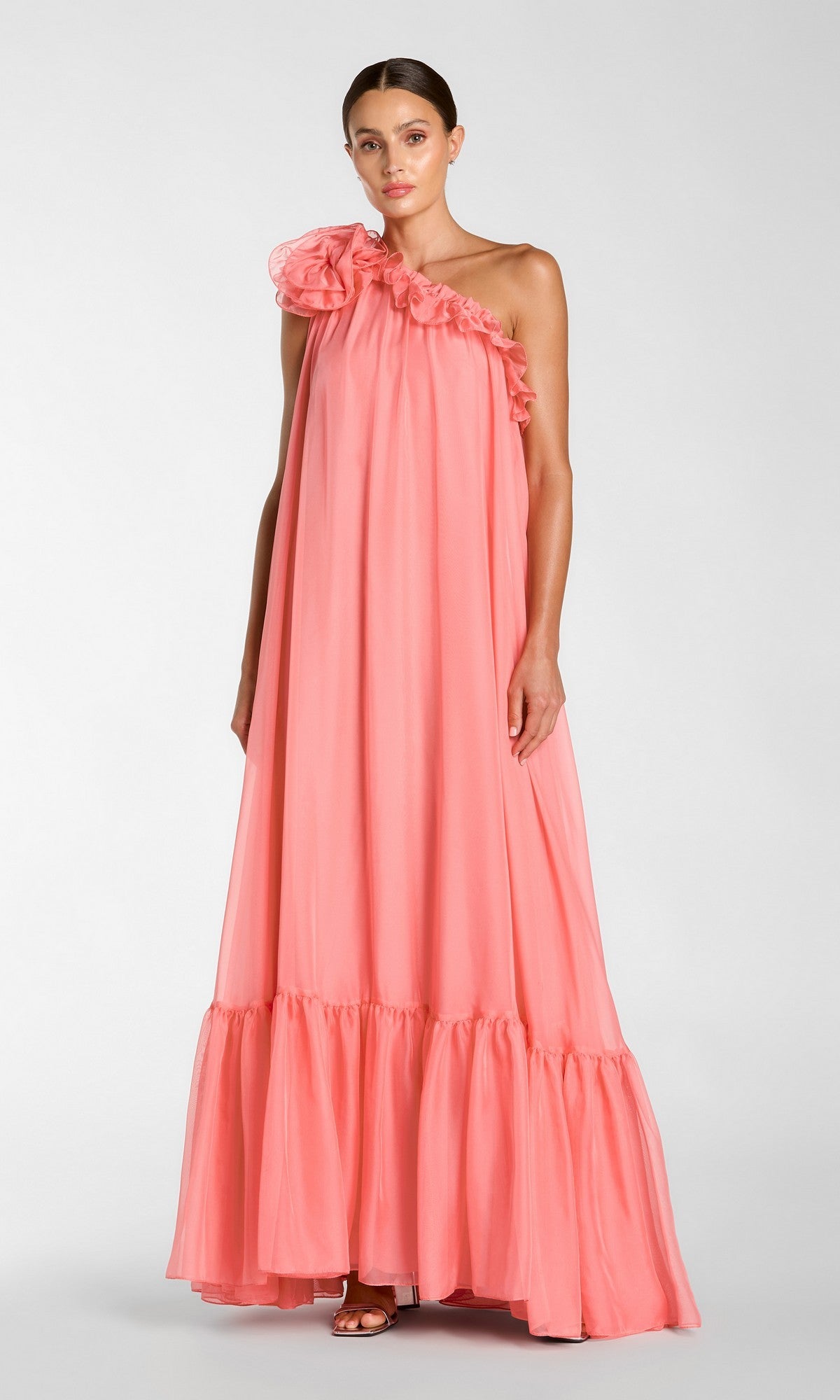 A woman stands against a plain light background wearing the Mac Duggal 68757 long formal dress in hibiscus, featuring a floor-length silhouette, sleeveless design, ruffled one-shoulder neckline, and gathered hem.