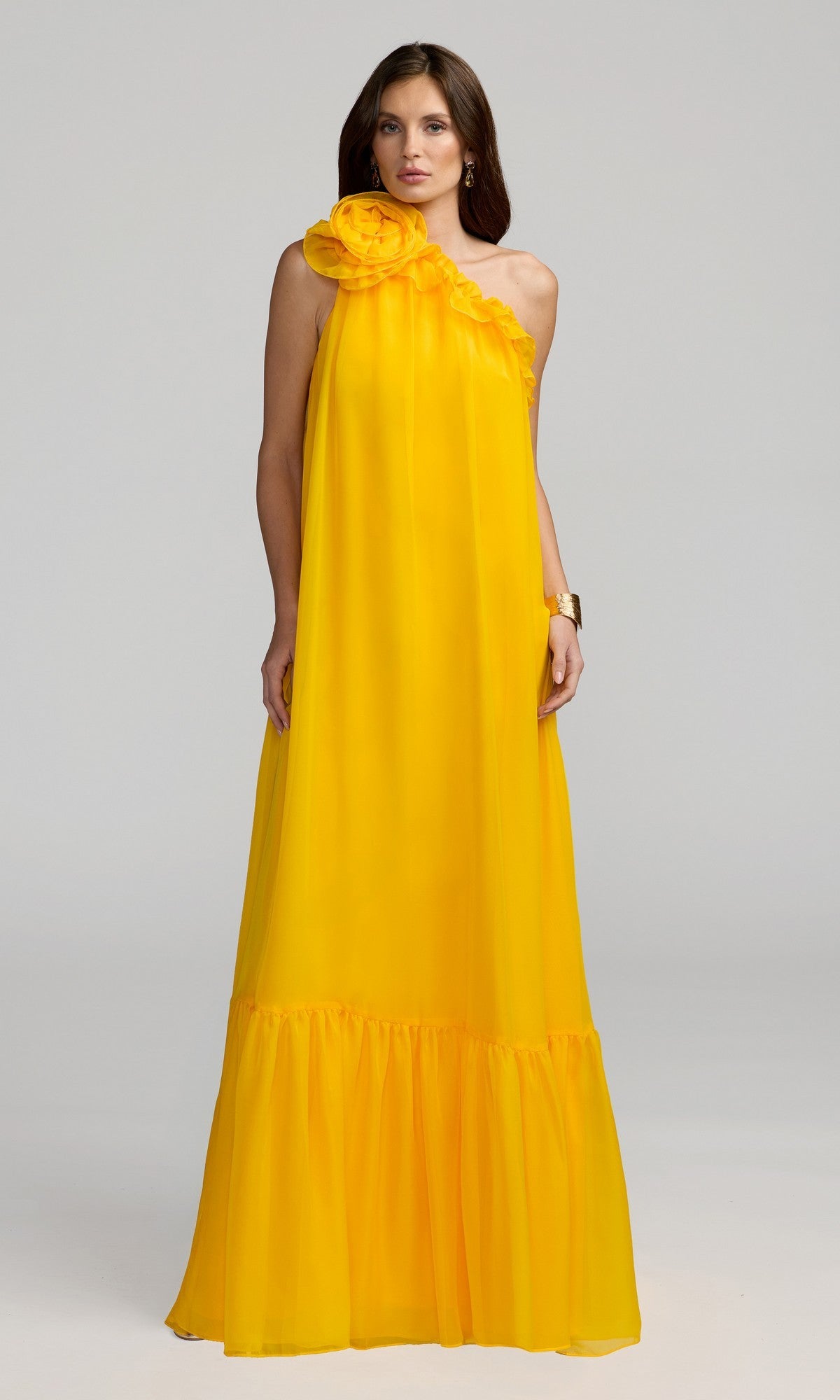 A woman stands against a plain light background wearing the Mac Duggal 68757 Long Formal Dress in Sunshine, a floor-length, one-shoulder chiffon gown featuring a ruffled neckline and gathered hem.