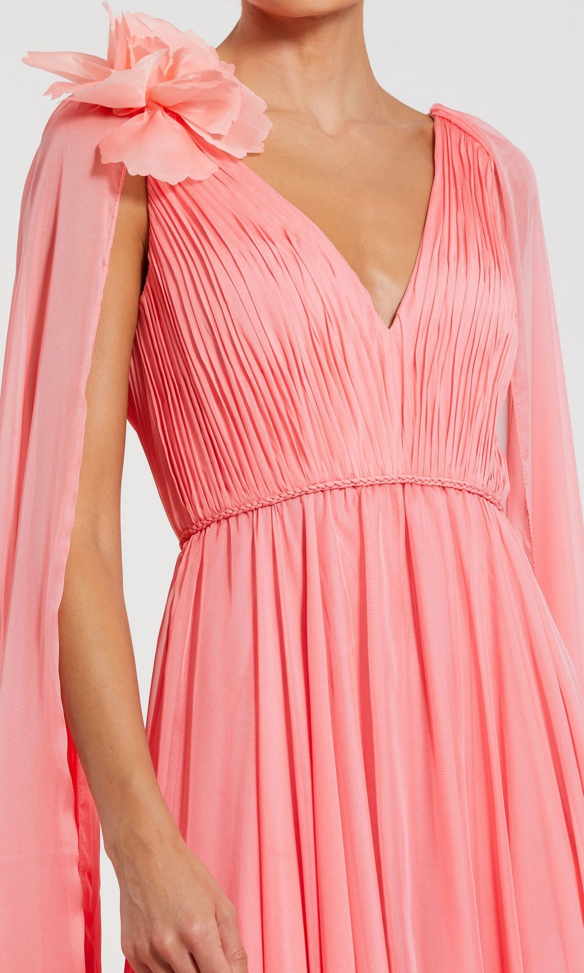 Wearing the Mac Duggal 68768 long formal dress, this person stuns in a pleated coral-pink chiffon gown with a deep V-neckline, floor-length cape sleeves, and a statement flower detail on the shoulder.