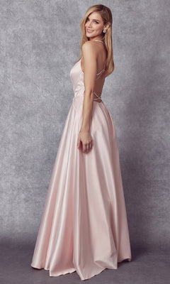 A woman smiles sideways in the Juliet 687 long prom dress—floor-length, light pink satin, open back, fitted bodice, and sheer v-neckline—posing against a gray textured background.
