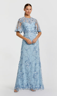 Woman wearing the Mac Duggal 68810 Flutter-Sleeve Long Formal Dress in light blue lace with floral appliqués, sheer flutter sleeves, and a high neckline—an ideal mother of the bride gown—posed against a plain light background.
