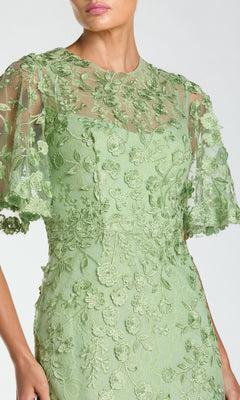 A woman in the Mac Duggal 68810 Flutter-Sleeve Long Formal Dress, featuring a light green color, floral embroidery, and sheer short sleeves.