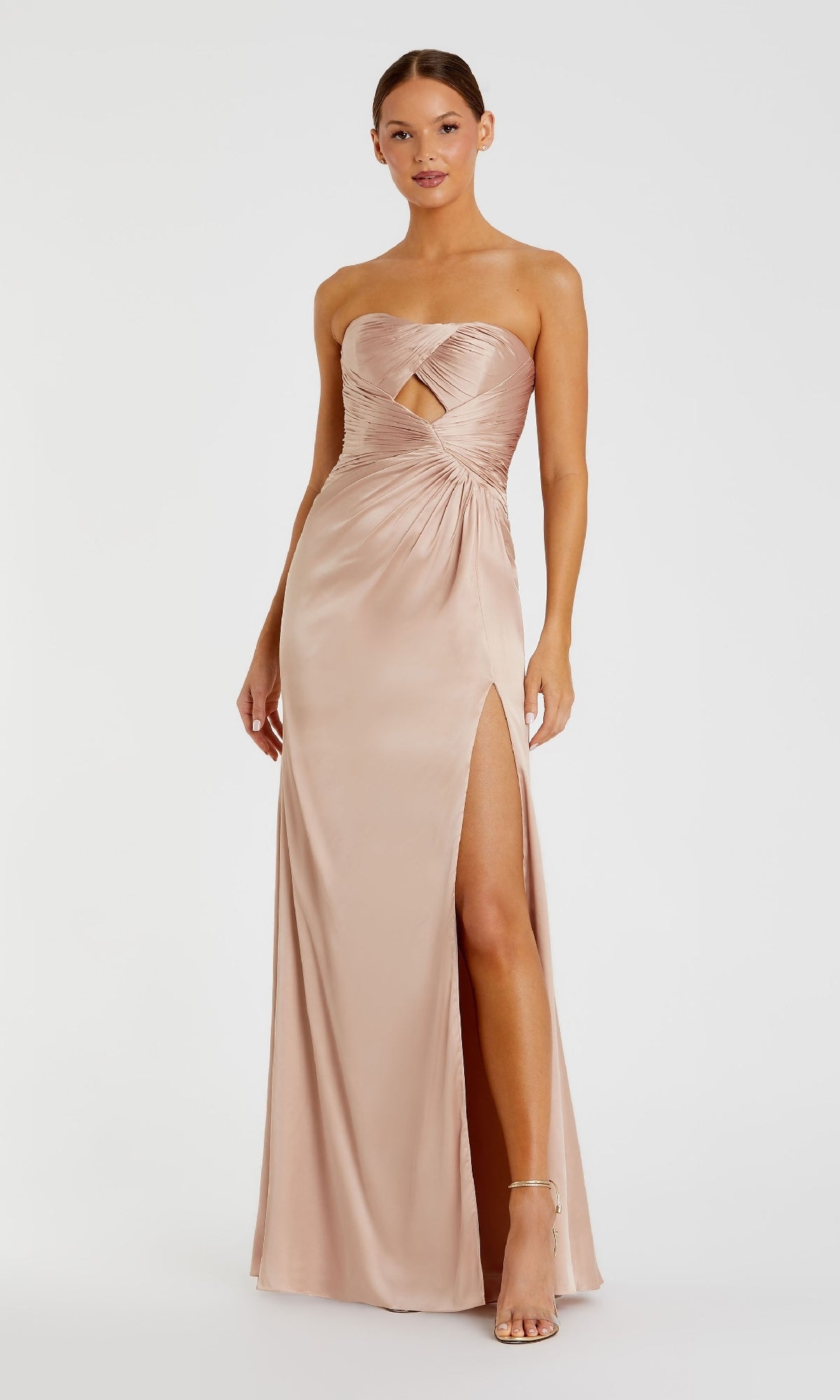 A woman stands against a plain white background wearing the Mac Duggal 68837, a strapless long formal dress in light beige satin featuring a front cutout, gathered bodice, high leg slit, and paired with strappy heels.