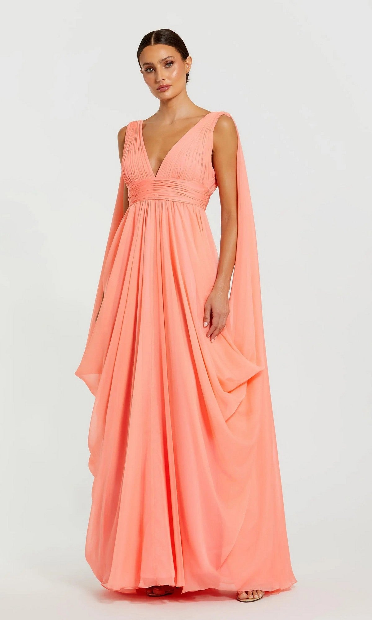 A woman poses against a plain background wearing the Mac Duggal 68860 long formal dress in coral—a floor-length, sleeveless chiffon gown featuring a deep V-neckline and draped fabric accents.