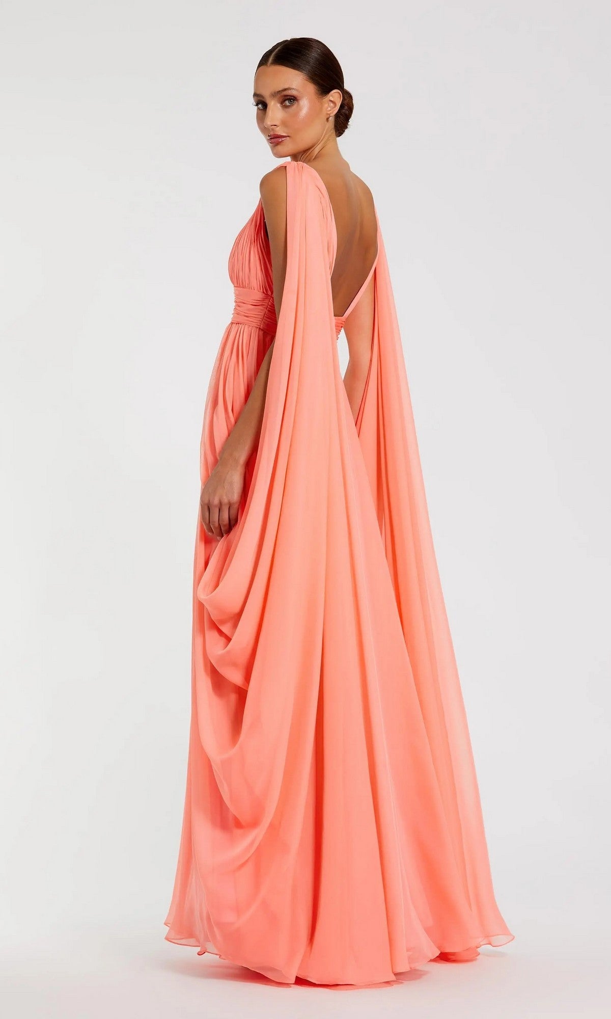 A woman wearing the Mac Duggal 68860 long formal dress—a floor-length, peach-hued gown with elegant draped cape sleeves—stands against a plain white background, gazing over her shoulder.