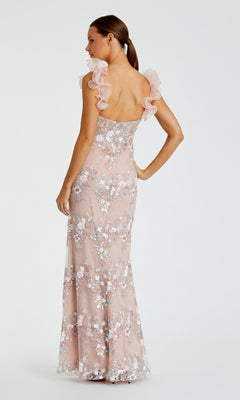 A woman stands with her back to the camera, wearing the Mac Duggal 68880 long formal dress—a light pink, floor-length gown featuring floral embroidery, sheer ruffled shoulder straps, and a bustier bodice.