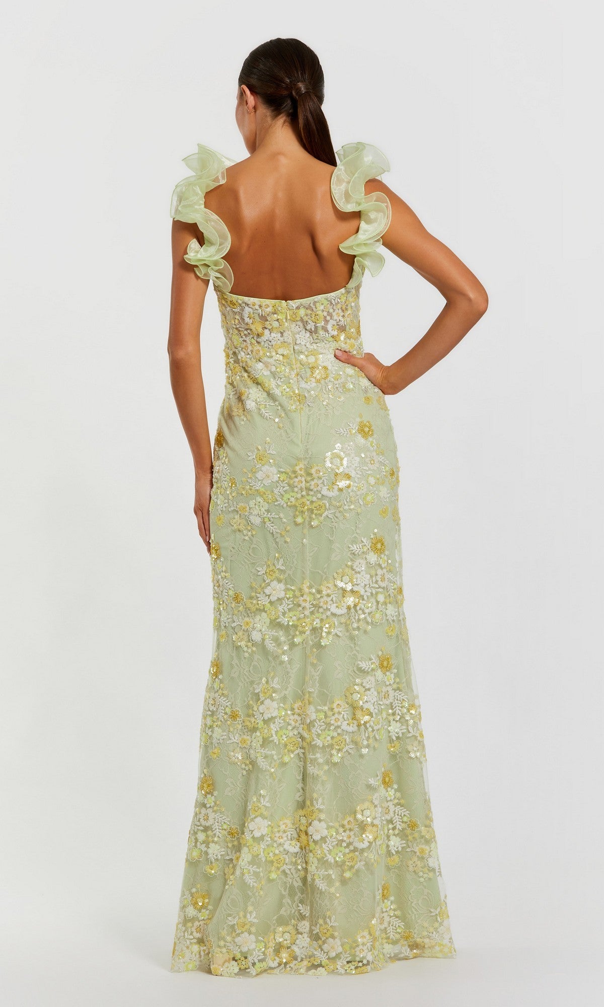 A woman with her back to the camera wears the Mac Duggal 68880, a long light green formal dress featuring floral embroidery and ruffled shoulder straps.