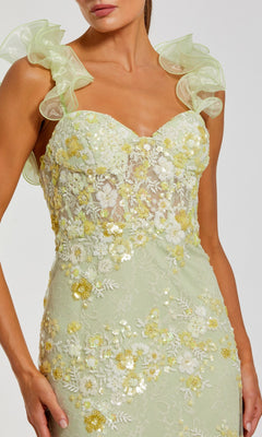 A woman wearing the Mac Duggal 68880 long formal dress featuring a light green hue, floral embroidery with yellow and white flowers, ruffled tulle shoulder straps, a sheer bodice, and a subtle sweetheart neckline.