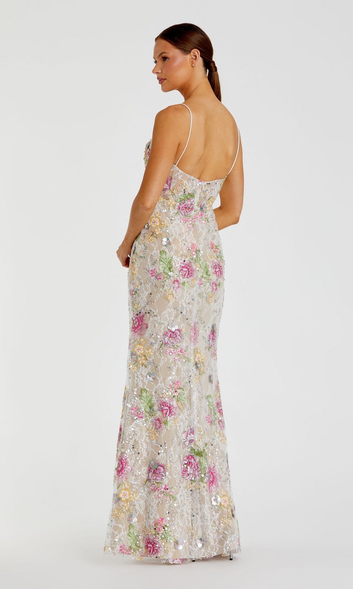 A woman stands facing away in the Mac Duggal 68891 long formal dress, featuring a sheer design with multicolored floral embroidery and thin straps, set against a plain white background.