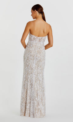 A woman stands facing away against a plain white background, wearing the Long Formal Dress: Mac Duggal 68893—a floor-length, form-fitting strapless gown featuring intricate white lace, shimmering sequin patterns, and delicate floral beadwork.