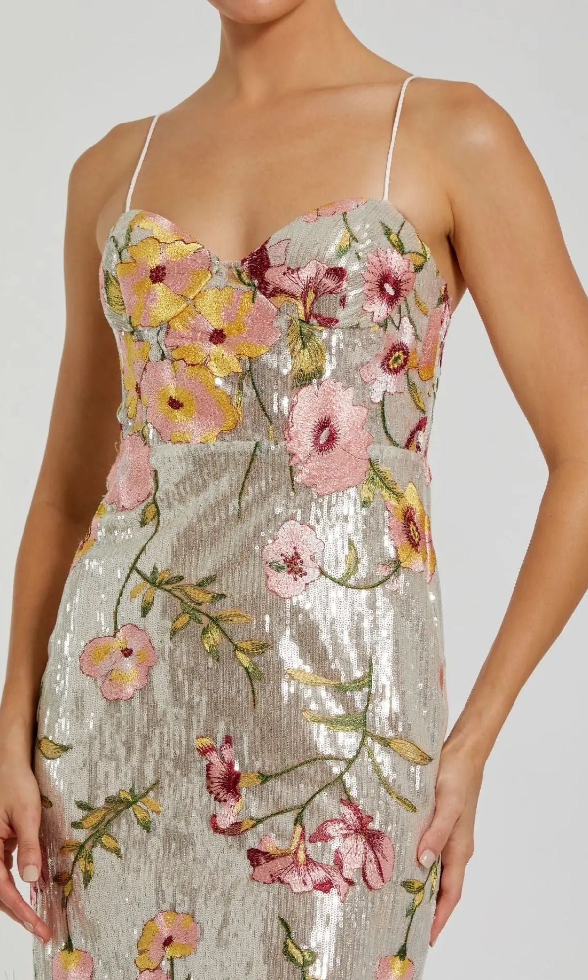 A woman wears the Mac Duggal 68896 long formal dress, a sleeveless silver sequin evening gown with thin straps and colorful floral embroidery.