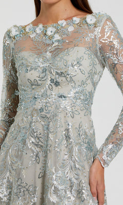 A woman wearing the Mac Duggal 68898 Midi Party Dress, featuring long sheer sleeves, silver and blue floral embroidery, delicate sequin embellishments, and 3D flower details along the neckline.