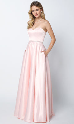 A woman modeling the Juliet 688 long prom dress, showcasing a strapless sweetheart neckline, light pink satin fabric, fitted bodice with beaded waistband, floor-length skirt, and pockets against a plain background.
