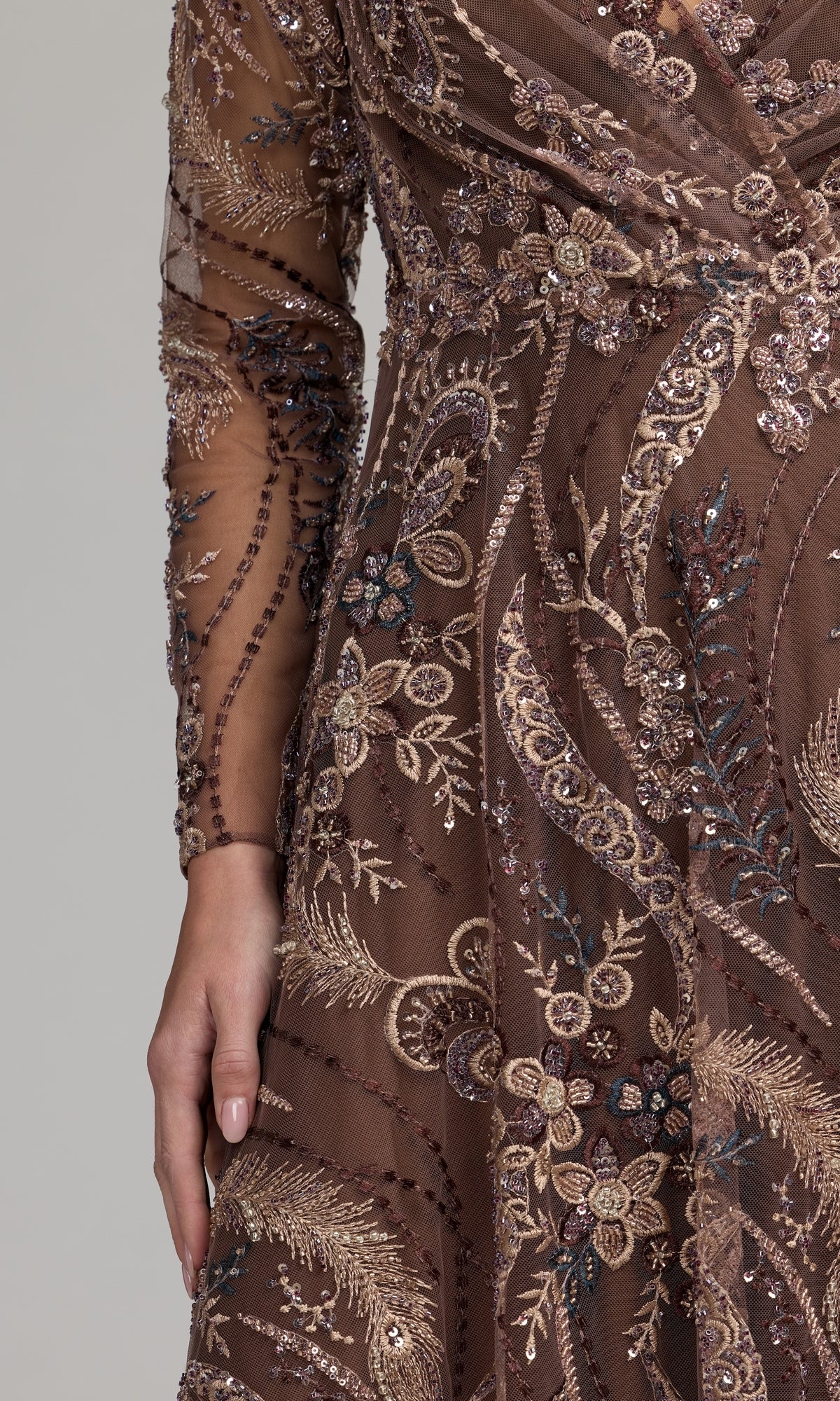 A person wearing a sheer, long-sleeved brown dress with intricate beaded and embroidered floral patterns evokes the elegance of the Mac Duggal 68906 Champagne Midi Party Dress.
