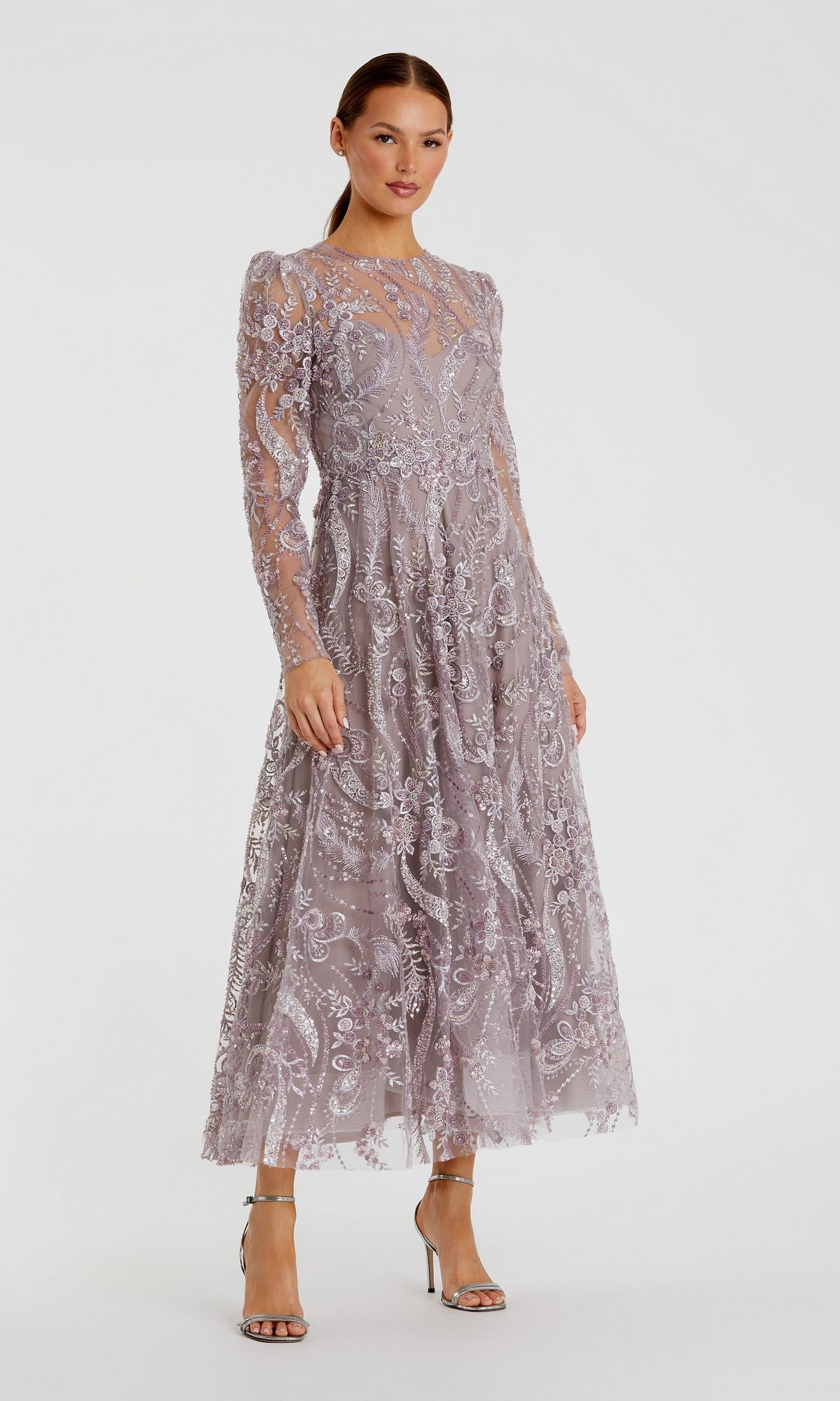 A woman stands against a plain background wearing the Mac Duggal 68910 Tea-Length Party Dress in mauve, featuring long sleeves, lace embroidery with floral embellishments, and sheer details. She completes the elegant look—reminiscent of Mac Duggal’s style—with silver high-heeled sandals.