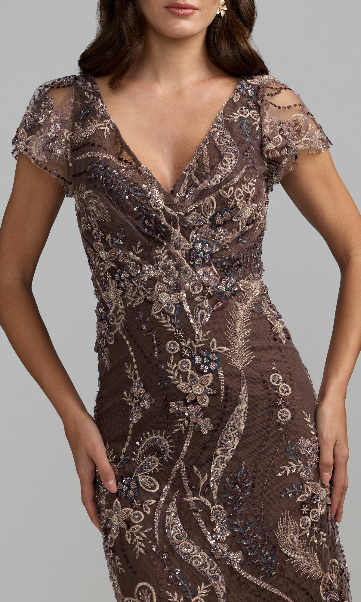 A woman wearing the Long Formal Dress: Mac Duggal 68914—a short-sleeve, V-neck evening gown featuring intricate beadwork and floral embroidery in brown and beige tones.