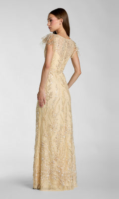 A woman stands facing away from the camera against a plain gray background, wearing the Long Formal Dress: Mac Duggal 68914—a floor-length, short-sleeved beige lace gown adorned with sequin detailing that reflects Mac Duggal’s signature elegant style.