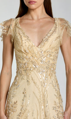 A woman wearing the Mac Duggal 68914 long formal dress in light gold, featuring intricate sequin and bead embroidery, sheer short sleeves, and a deep V-neckline.