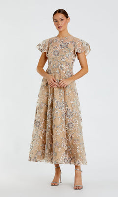 A woman wearing the Mac Duggal 68920 Tea-Length Party Dress in nude, featuring floral embroidery and short flutter sleeves, paired with silver high-heeled sandals, stands against a plain white background.