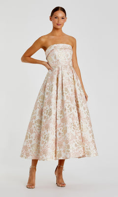 A woman poses against a plain white background in the Mac Duggal 68928 long formal dress, featuring a strapless fitted bodice and pleated skirt, styled with nude high-heeled sandals.