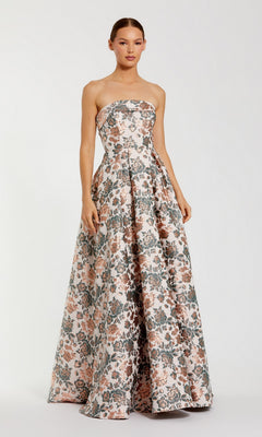 A woman stands against a plain white background wearing the Mac Duggal 68945 long formal dress, a strapless ball gown in a gold multi brocade floral pattern.