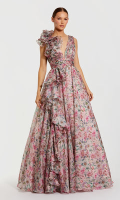 A woman wears the Mac Duggal 68947: a floor-length, sleeveless formal dress with a pink floral print, deep V-neckline, and asymmetric ruffled details on the bodice and skirt.