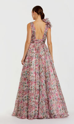 A woman faces away in the Mac Duggal 68947 floral-print long formal dress, featuring chiffon fabric, a deep V-back, and a shoulder bow—an elegant choice for prom.