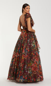 A woman stands facing away from the camera in the Mac Duggal 68947, a long floral-print formal dress with ruffled sleeves and an open back, capturing a sense of timeless elegance.