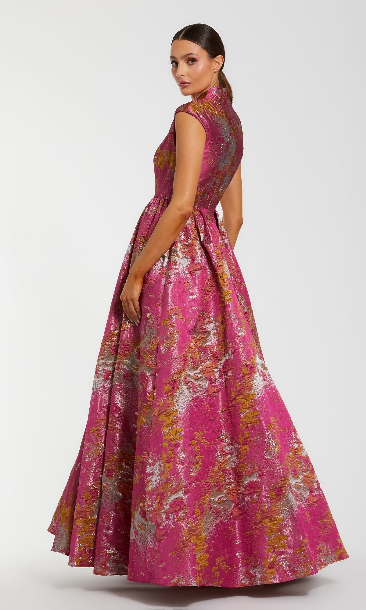 A woman models the Mac Duggal 68956 long formal dress, featuring cap sleeves and a pink, gold, and silver metallic floral pattern with an elegant A-line skirt, against a simple light background.