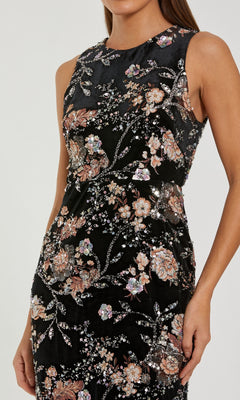 A woman wears the Midi Black Wedding Guest Dress: Mac Duggal 68958, a sleeveless black midi dress with a fitted waist and pink, beige, and silver floral sequin embroidery.