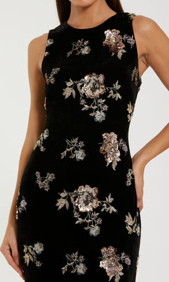 A woman wears the Black Velvet Print Formal Dress by Mac Duggal (style 68959), featuring metallic floral embroidery and sequin accents.