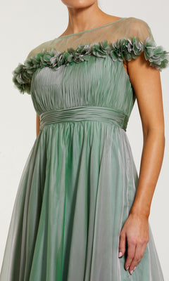 A woman wearing the Mac Duggal 68966 tea-length party dress in light green, featuring an off-shoulder fit-and-flare silhouette with a ruched bodice, sheer neckline, and floral detailing along the top edge.