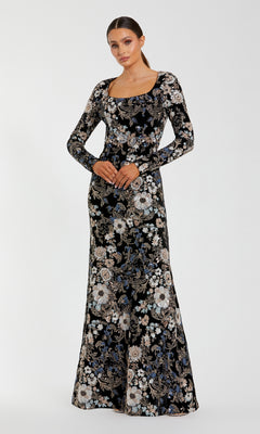 A woman stands facing forward in the Mac Duggal 68978 Black Velvet Print Formal Gown, featuring an intricate embroidered sequin floral print, hands gently clasped at her waist.