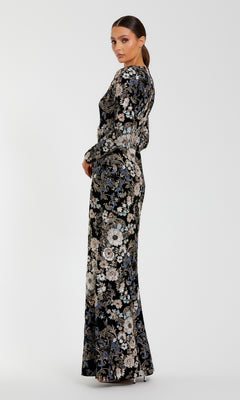 Woman wearing the Mac Duggal 68978 Black Velvet Print Formal Gown with long sleeves, floor length, embroidered sequin floral print, and side slit, standing sideways against a plain white background.