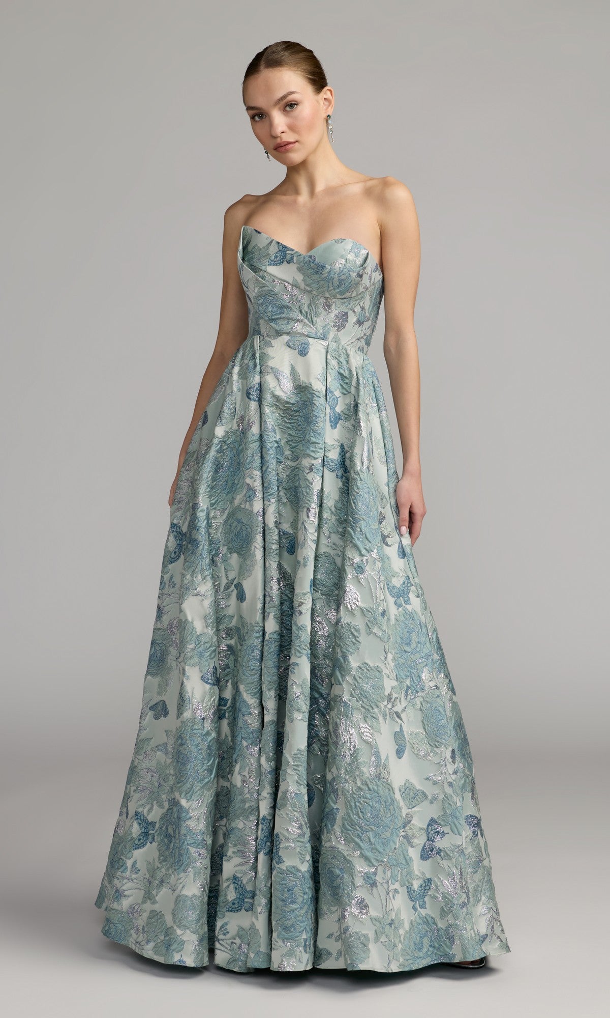 A woman wearing the Long Formal Dress: Mac Duggal 68999—a strapless, floor-length brocade ballgown in seafoam with a delicate floral pattern—stands against a plain gray background.