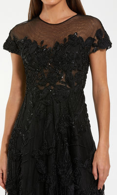 A woman wearing the Cap-Sleeve Black Formal Dress: Mac Duggal 69003, featuring floral embroidery, beaded details, sheer fabric, short sleeves, and a fitted waist—a stunning choice for formal evenings.